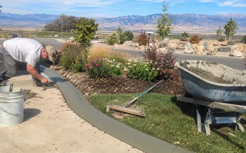 Fresh concrete curbing being finished with a trowel along a curved garden bed edge