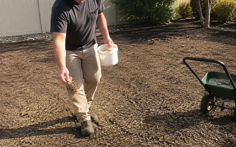 Hand spreading grass seed across prepared soil in a Utah yard