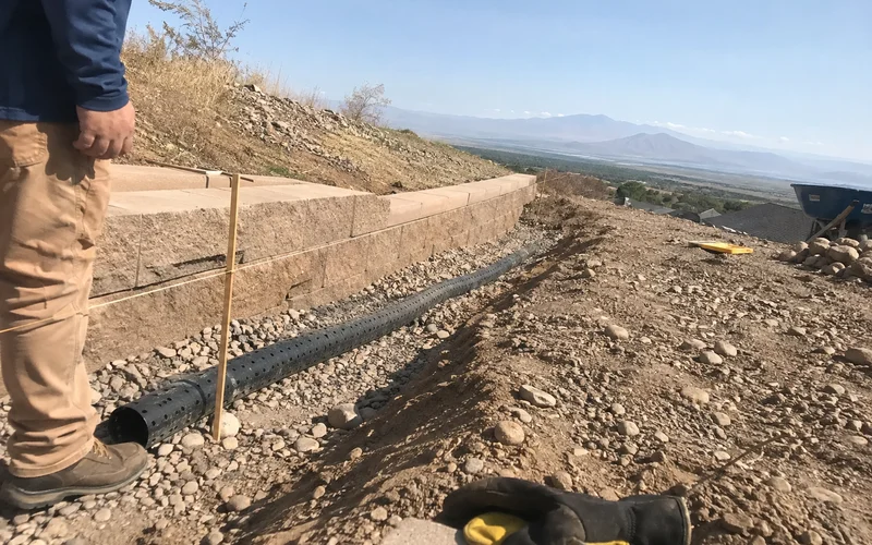 Perforated drain tile laid in clean gravel behind a retaining wall base course