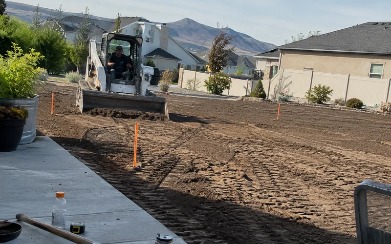 Skid steer finish-grading a residential Utah yard with grade stakes set