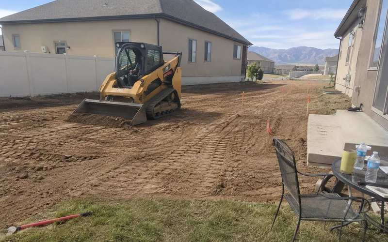 Skid steer regrading a residential Utah yard to create positive drainage away from the home