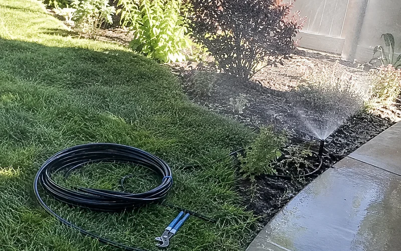 Spray sprinkler misting over a garden bed edge and onto a path