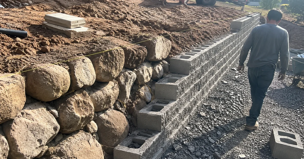 Engineered block retaining wall beside a decorative natural boulder rock wall in the same yard
