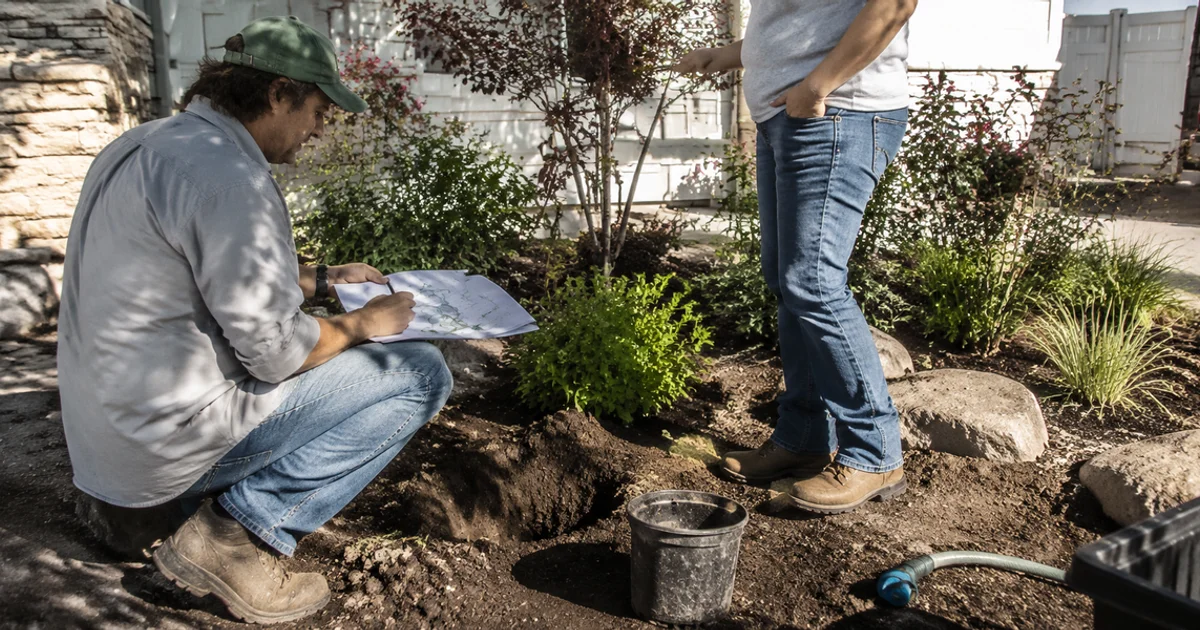 Landscape designer sketching a yard plan on site with a homeowner in a Utah garden