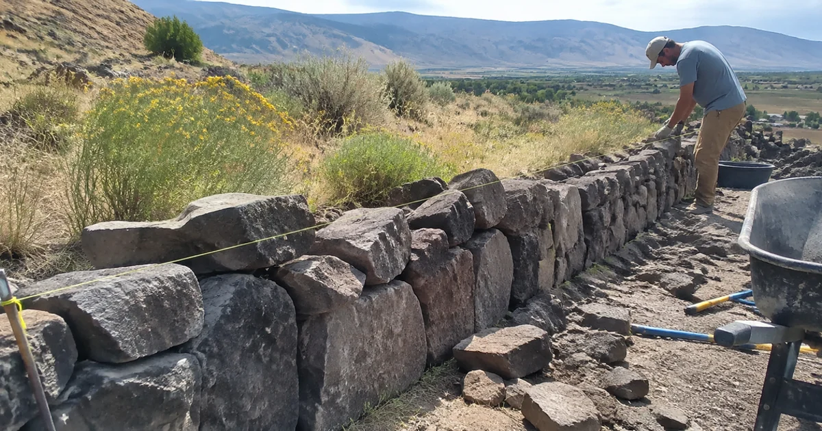 Natural basalt boulder wall running through a rural Utah landscape with planting between the stones