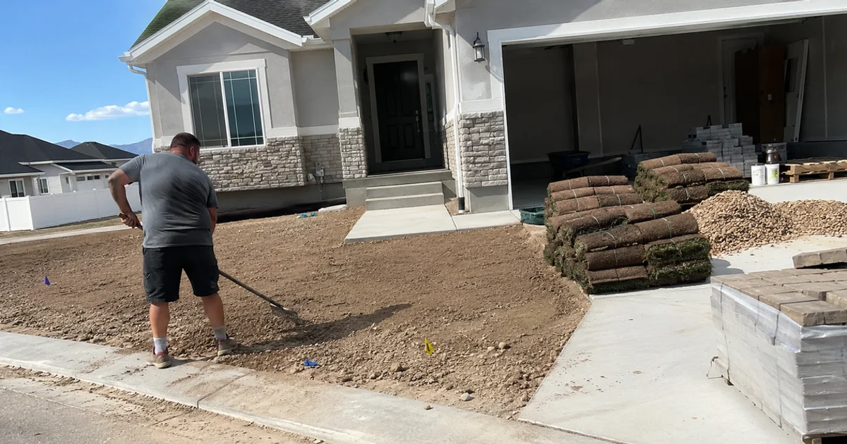 A new-build Utah home with a bare dirt front yard mid-install and landscaping materials staged on the driveway