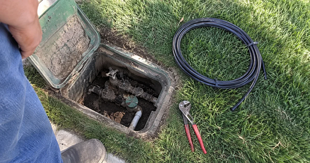 Old corroded sprinkler valve box with aged fittings beside a green Utah lawn