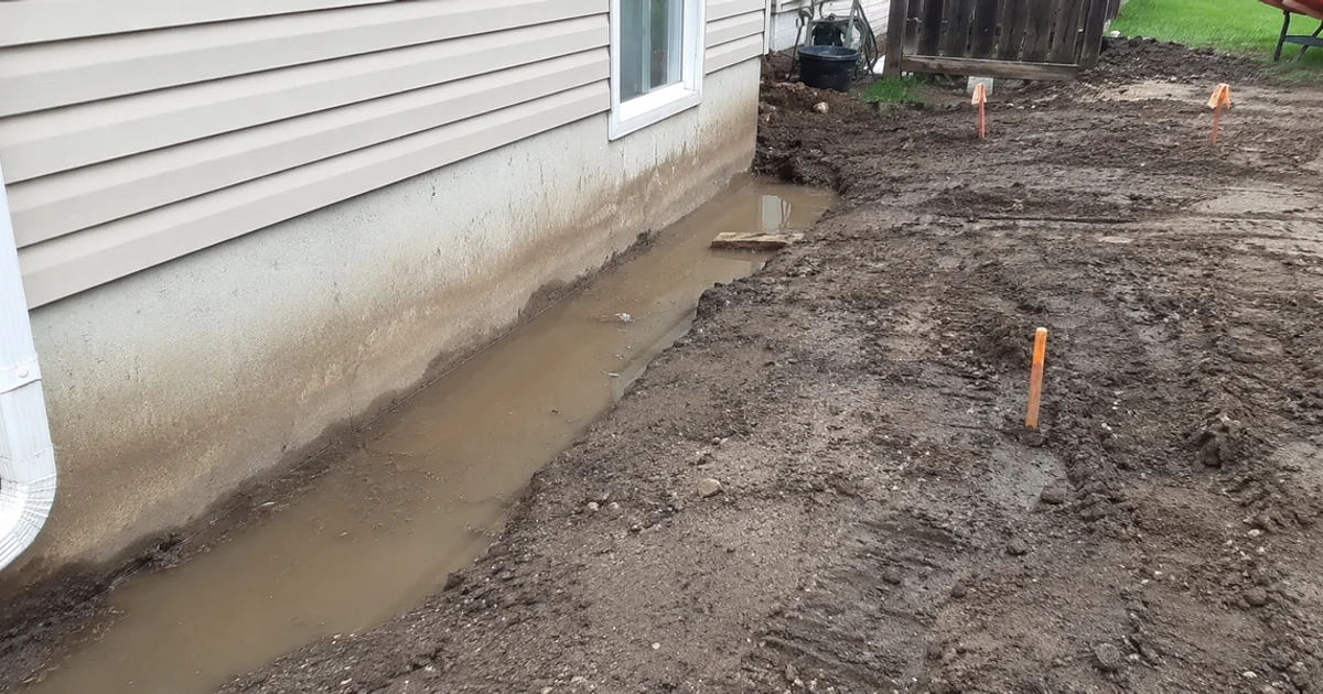 Water pooling against a house foundation in a poorly graded Utah yard after a storm