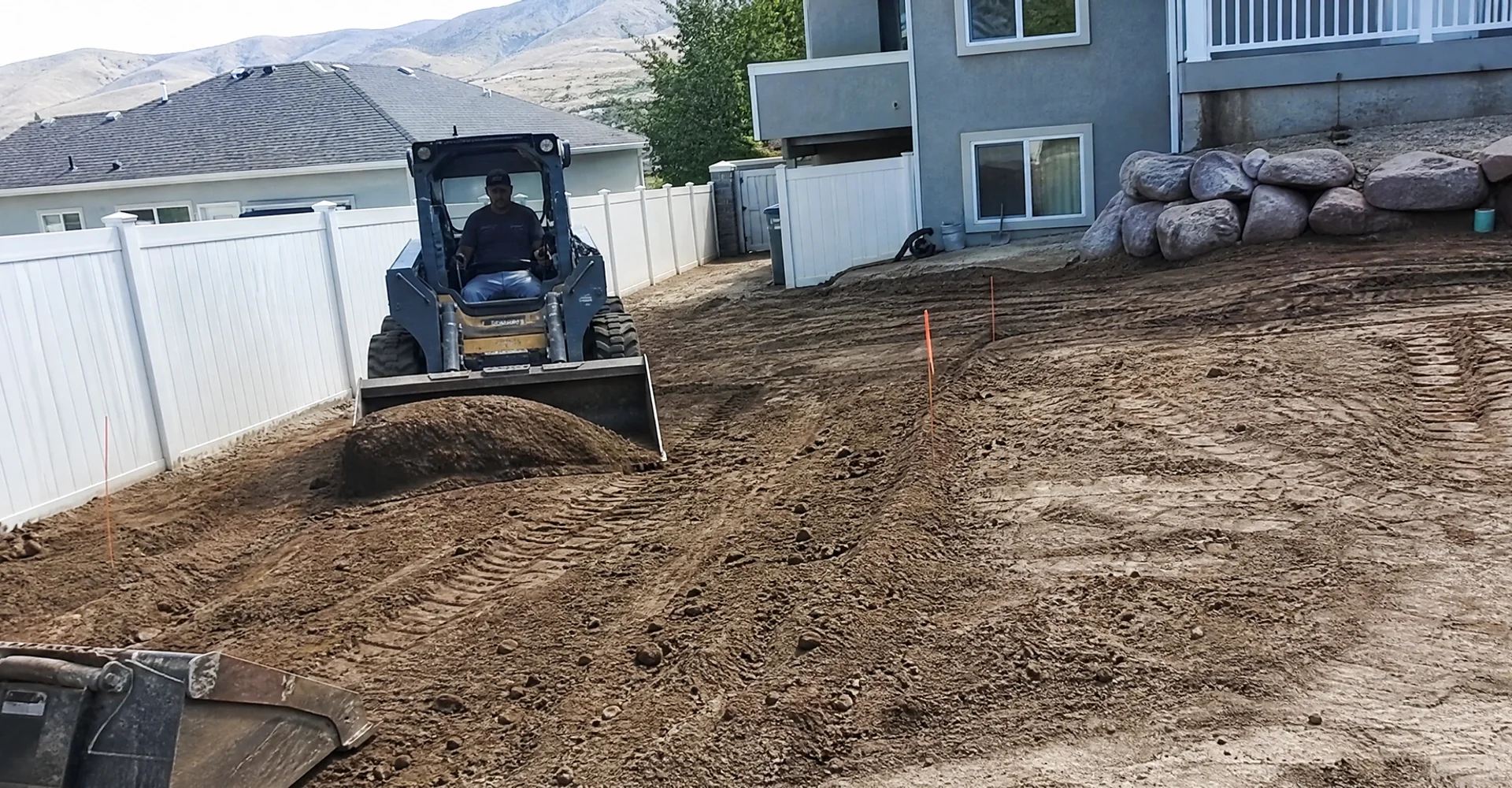 Skid steer finish-grading a residential Utah yard to create positive drainage away from the house
