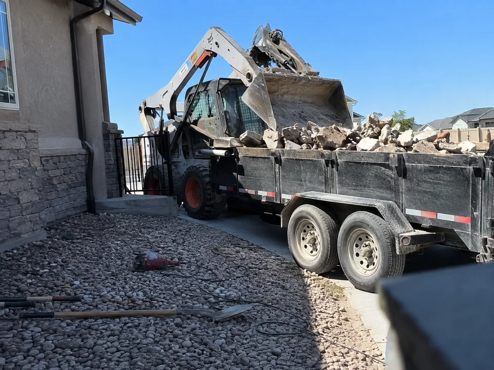 Skid steer loading broken hardscape debris into a dump trailer at a residential Utah property